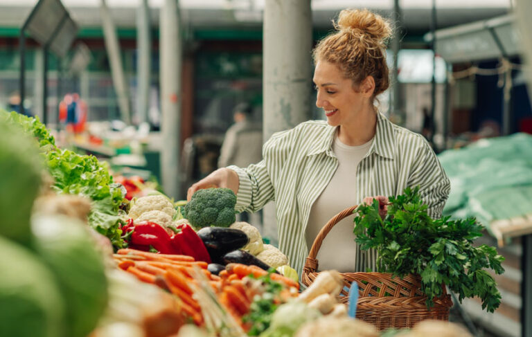 Lebensfrohe Frau mit Einkaufskorb am Wochenmarkt – steht für bewusste Ernährung und Lebensqualität bei Diabetes.